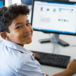 Photo of a school boy in classroom studying coding with his computer.